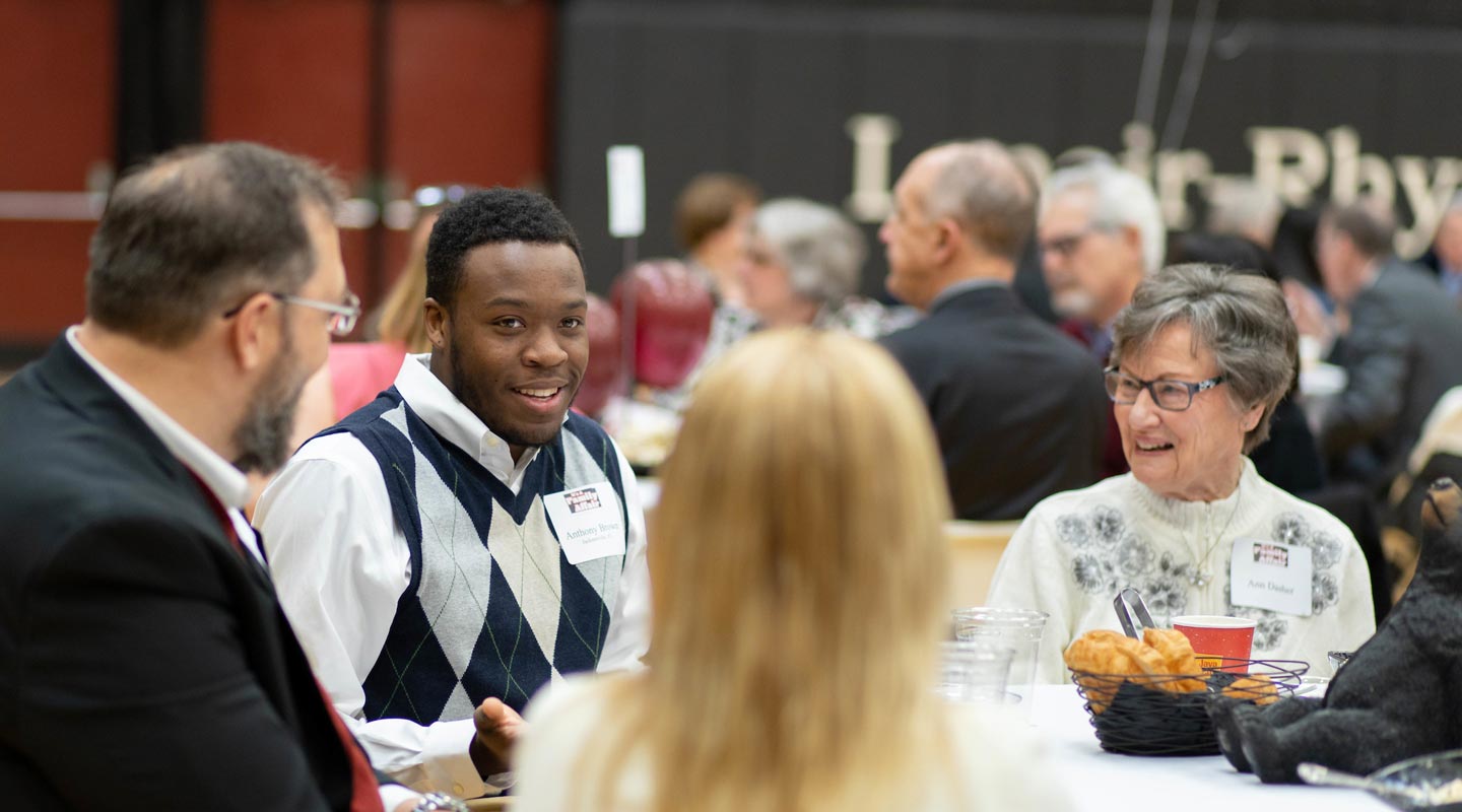 A scholarship recipient talks with scholarship donors at luncheon table