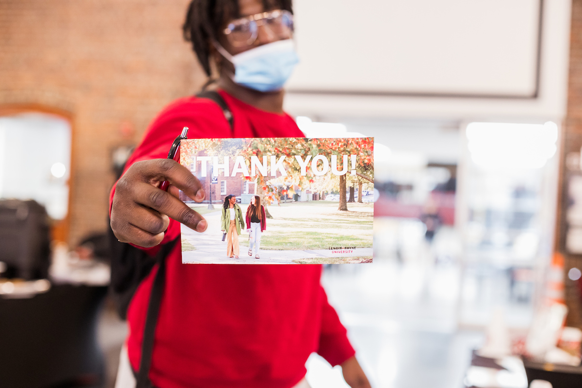 A masked student holds out a thank you postcard to the camera