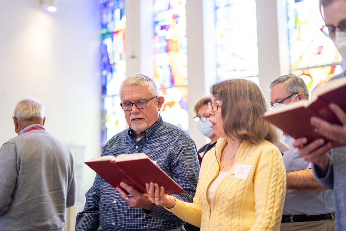 Alumni stand in chapel and read from the hymnal