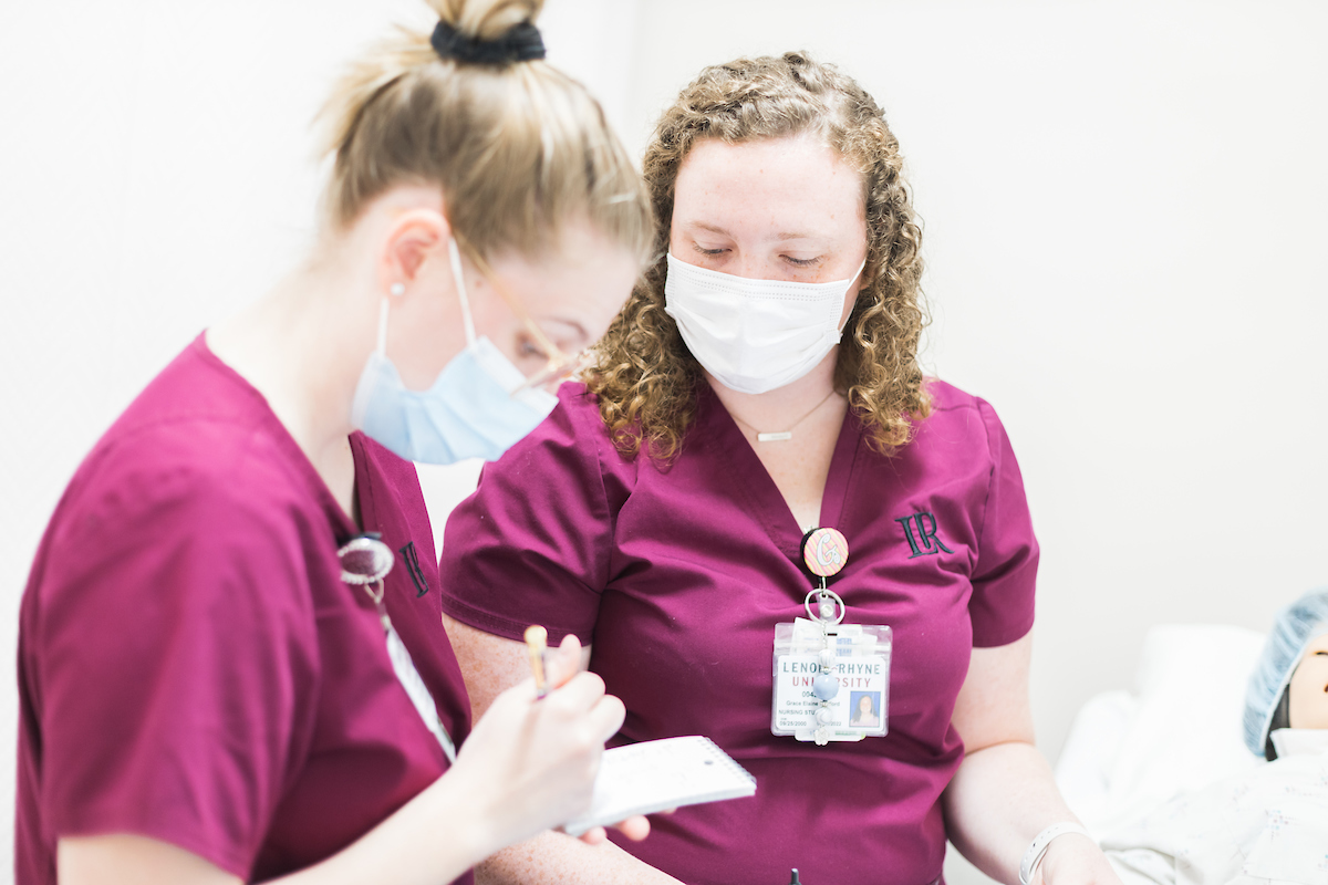 Two masked female nursing students stand and look at a notecard 