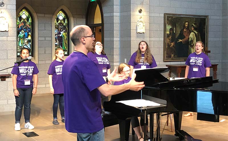 Choir director Ryan Luhr leads a practice with young summer camp singers