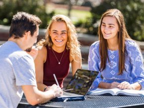 Three people sit at an outside picnic table