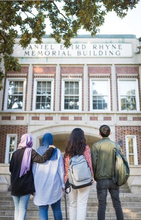 Four students with their backs to the camera look at Rhyne Building