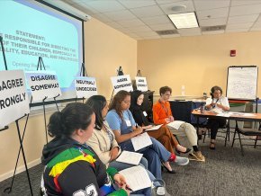 Students sit in a row in front of a screen and a series of placards in a dialogue training session