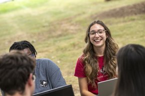 A small group of students sits outdoors with laptops while working together