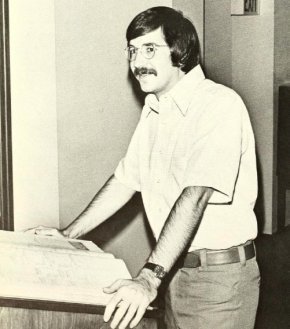 Burl McCuiston stands with a reference book at a podium in 1976