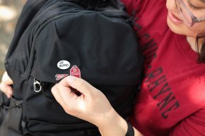 Student displays three enamel pins on a backpack in closeup