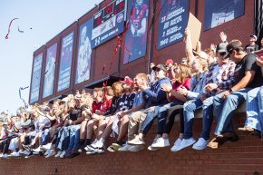 Students cheer from the student section in Moretz Stadium with brick wall and football banner above and behind them