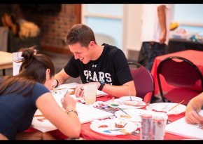 Isaac Riggs paints a canvas at a table with other students at a CAB event