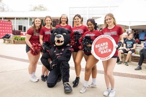 Students pose with Joe Bear and Bears Give Back signs in front of Cromer Center