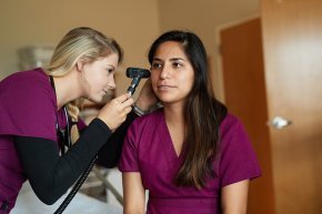 Nursing student uses a scope to look in another student's ear