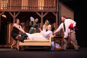 3 performers gather around an actor reclining on a couch on stage during a performance