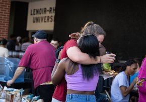 Twi students hug in greeting by the serving table at the President's Cookout