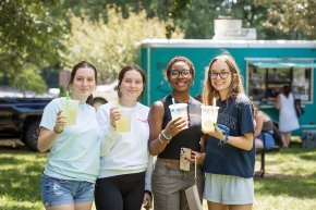 Four students raise their lemonade in front of a food truck