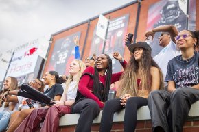 Students sit on the wall of the student section in Moretz Stadium and cheer for the football team