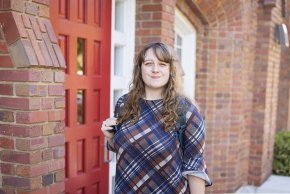 Elise Prouty stands outside the red door at the main entrance to Mauney Hall