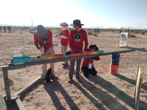 Three rocketry team members prepare the rocket for launch on a platform in the desert