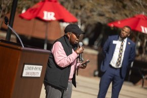 Margart Pope stands before a podium with a microphone in hand on Shaw Plaza