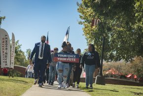 A group of LR students, faculty and staff walk down a sidewalk away from Shaw Plaza, holding a sign in front that reads "Your Voice, Your Vote"