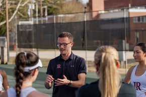 Coach Sam Clarke talks to members of the tennis team on the court