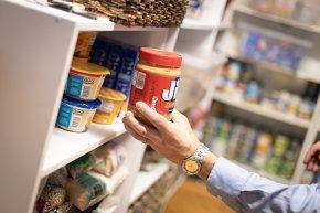 A hand places a jar of peanut butter on a shelf in the LR food pantry.