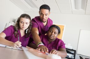 Three nursing students wearing scrubs work together at a table 