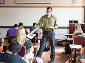 A masked professor hands out papers to masked students on the first day of classes.