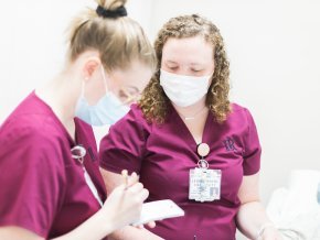 Two masked female nursing students stand and look at a notecard 