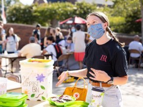 Kaley Cross works an information table outside while wearing a mask