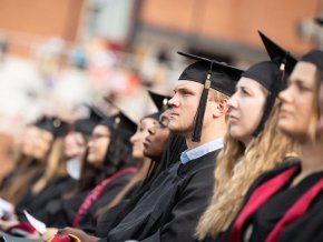 Graduates in crowd listen to speakers on commencement stage