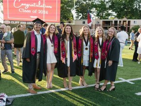 Six students in graduation regalia stand on the field under a sign reading "Congratulations Class of 2024"