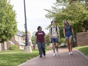 Three students walking across campus with Grace Chapel and Shaw Plaza in the background