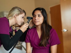 Nursing student uses a scope to look in another student's ear