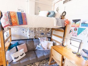 Interior of a dorm room with a sofa below loft bed, light strings and colorful throws and pillows