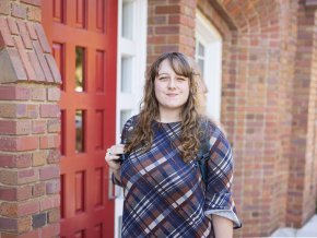 Elise Prouty stands outside the red door at the main entrance to Mauney Hall