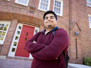 Raj Donepudi stands in front of the red main door at Mauney Hall