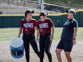 Two softball players laugh on the field with Coach Shena Hollar