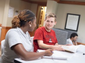 Two students look at each other while studying indoors