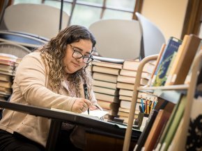 Lizbeth Santibanez works at a table surrounded by books in Rudisill Library