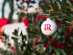 A white christmas ball with red LR logo hangs in a holly tree