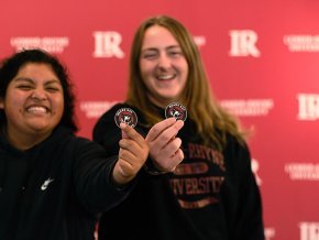 In front of red backdrop with LR logo visible, two female students hold out Bears Say Thanks stickers to foreground