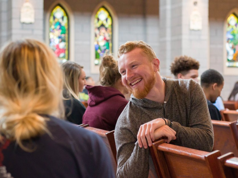 A student looks back at other while talking and smiling in chapel. 