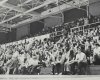 A group of students watch a basketball game indoors in a black and white 1973 archive photo