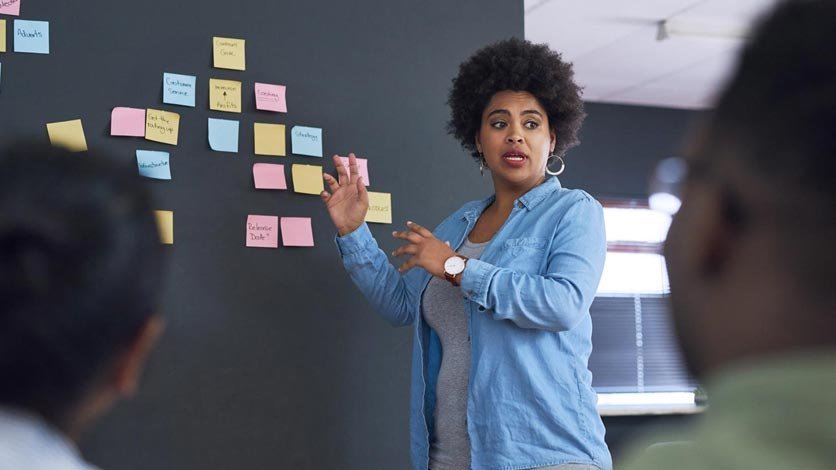 Instructor teaching at front of class pointing to post it notes